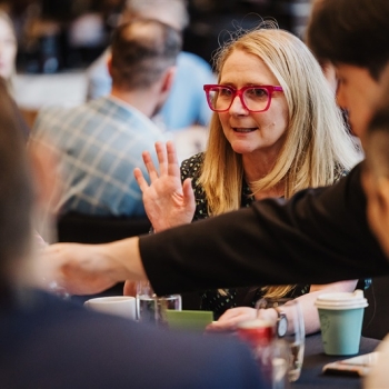 Steph Ransom, with bright pink glasses speaks with energy during a roundtable discussion at Design Leadership 2025, surrounded by engaged peers.