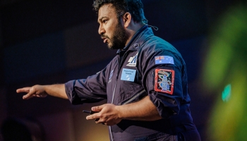Dwayne Fernandes, wearing a space-themed flight suit, presenting passionately on stage at Accessibility & Inclusion 2025, gesturing with intensity.