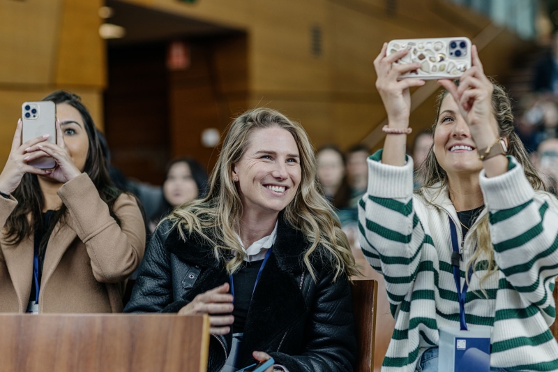 Three attendees at Design Outlook 2022 seated in the audience, smiling and capturing moments on their phones during a session.