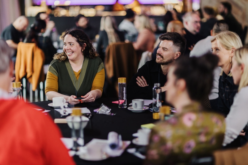 Group of people smiling and chatting around a table during a workshop or roundtable session.