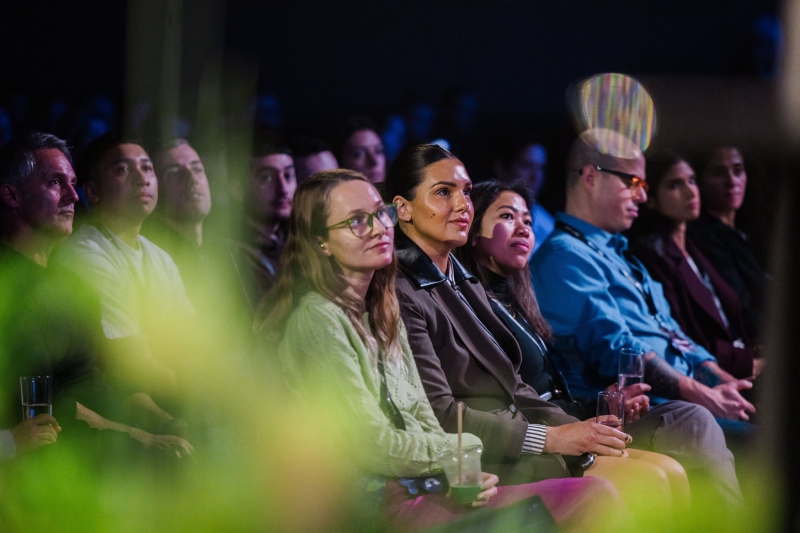 Audience members at Design Outlook 2025 seated and listening attentively to a presenter, with soft lighting and greenery in the foreground.