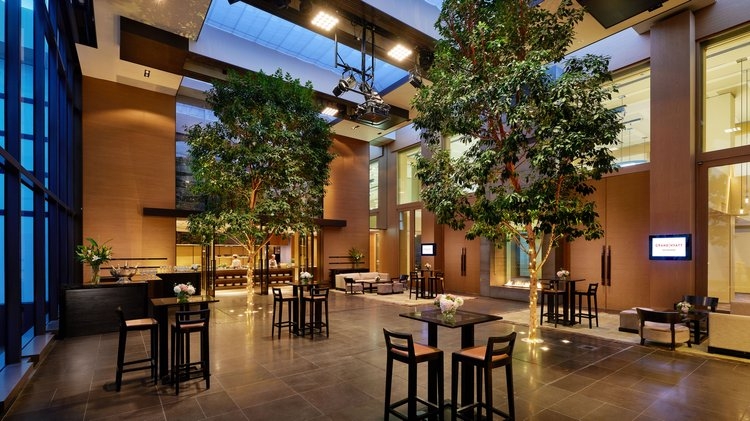 The Residence at Grand Hyatt Melbourne, a sophisticated indoor event space with high ceilings, indoor trees, modern furniture, and warm ambient lighting.