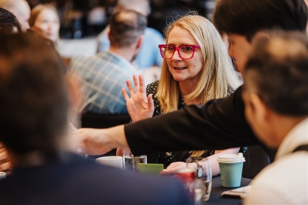 Steph Ransom, with bright pink glasses speaks with energy during a roundtable discussion at Design Leadership 2025, surrounded by engaged peers.