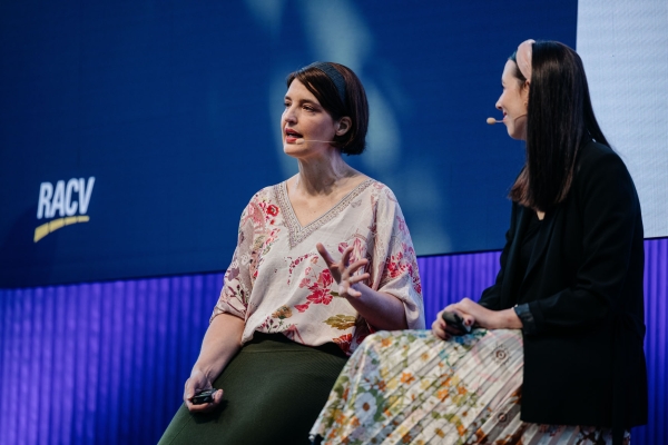 Nicole Austin and Louise Sporton sit onstage at Design Outlook 2022. Nicole wears a floral blouse; Louise wears a floral skirt and black blazer.