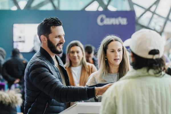 Attendees smiling and queuing at Design Outlook check-in, with a large purple abstract sculpture in the background and phones in hand.