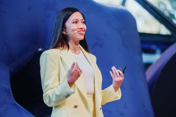 Berlin Liew, Design Outlook 2023 MC, speaking on stage in a yellow suit with a headset mic and remote clicker.