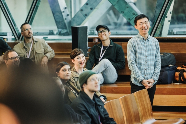 Audience members at Design Outlook 2023 seated in wooden-tiered seating, smiling and reacting during a session.