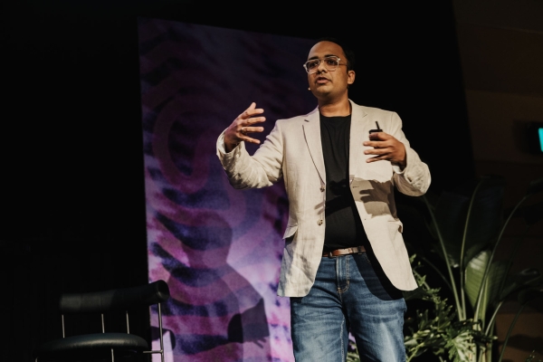Presenter Vivek Agarwal on stage at Design Outlook 2024, speaking animatedly in front of a bold purple backdrop and lush greenery.