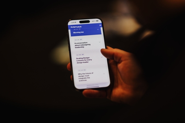 An attendee viewing the Design Leadership 2025 event schedule on their mobile phone, showing session titles and times on a dark background.