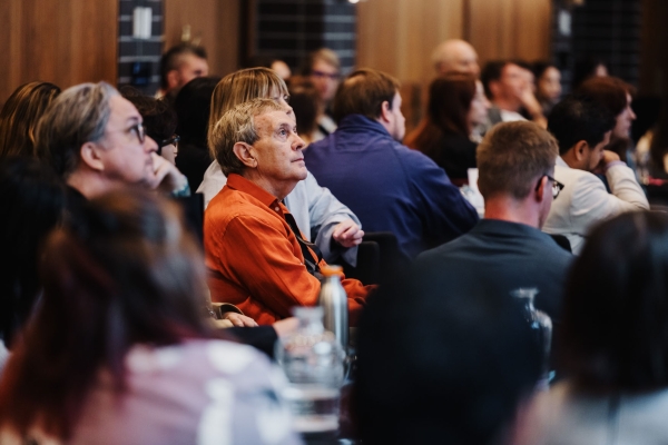 An attendee in an orange shirt listening intently during a session at Design Leadership 2025 in Melbourne, surrounded by a full room of participants.
