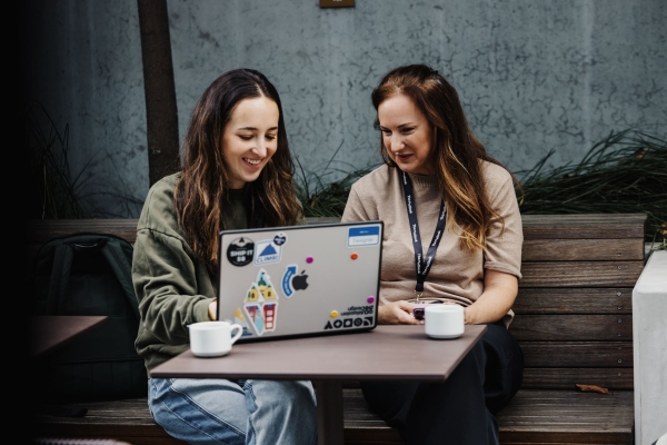 Two attendees using a laptop during the morning tea break at Design Leadership 2025 in Melbourne, seated outdoors with coffee cups on the table.