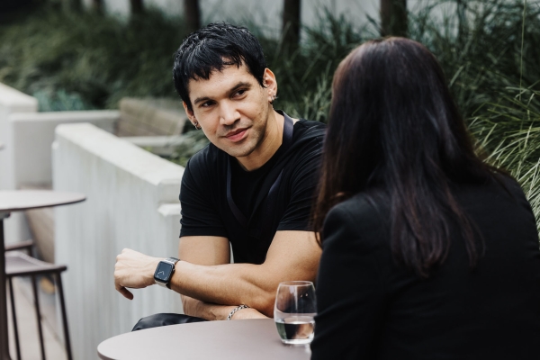 An attendee speaking with another person during a break at Design Leadership 2025 in Melbourne, seated outdoors with a glass of water on the table.