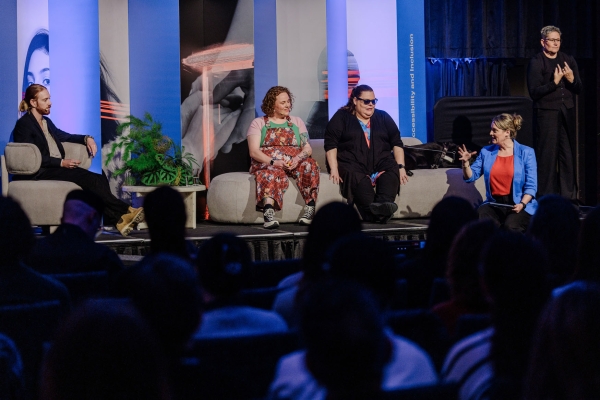 A diverse panel discusses accessibility and inclusion on stage at The Outlook, accompanied by an Auslan interpreter standing beside them.