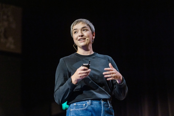 Presenter Georgia Rust speaking on stage at Product Outlook 2025, holding a clicker and wearing a headset mic during her talk.