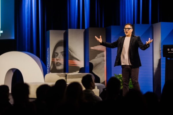 Simon Banks energises the crowd at The Outlook, presenting on stage with expressive gestures against a bold, modern backdrop.
