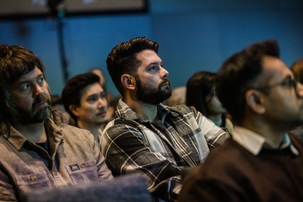 A man in the audience listening attentively during a Product Outlook 2025 session. Seated in the front row and wearing a grey plaid shirt, he reflects the focused and thoughtful energy of attendees throughout the day. Other audience members can be seen around him, all engaged with the presentation on stage.