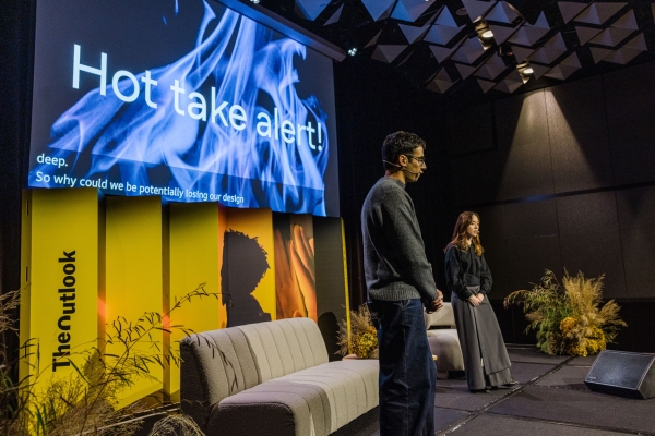 Presenters Larissa Francis and Zac Gandolfo standing on the Product Outlook 2025 stage in Melbourne, with a projected slide behind them reading “Hot take alert!” above blue flames.