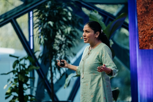 Sharbani Dhar presenting on stage at Design Outlook 2022, speaking passionately with a microphone headset in front of a lush, plant-filled backdrop.
