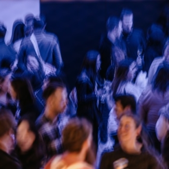 A bustling crowd at a Design Outlook event captured with an artistic, motion-blurred effect, creating a sense of movement and energy in the room.