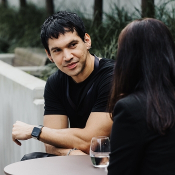 An attendee speaking with another person during a break at Design Leadership 2025 in Melbourne, seated outdoors with a glass of water on the table.