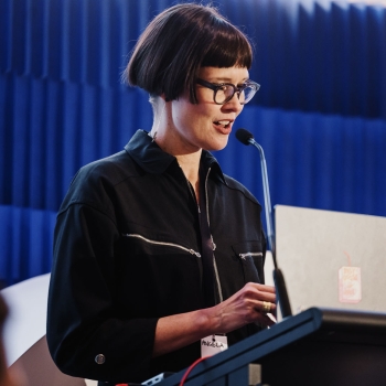 Presenter Angela Bliss speaking at the podium during Design Leadership 2025 in Melbourne, with a laptop and microphone in front of her.