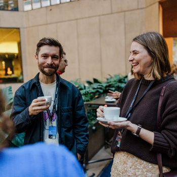 Two attendees enjoy coffee and conversation during a break at The Outlook, smiling and relaxed in the venue’s open-air atrium.