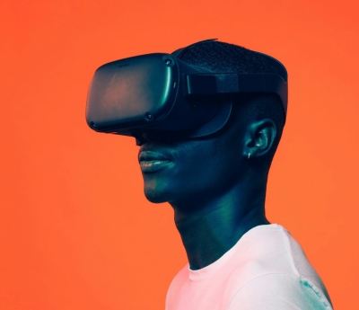 A man wearing a virtual reality headset stands against an orange background, his face illuminated with a soft blue tint