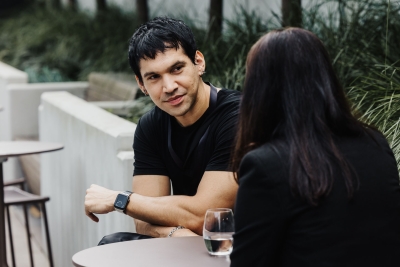 An attendee speaking with another person during a break at Design Leadership 2025 in Melbourne, seated outdoors with a glass of water on the table.