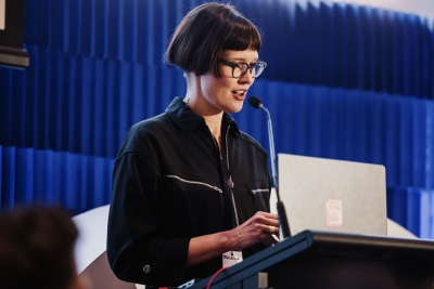 Presenter Angela Bliss speaking at the podium during Design Leadership 2025 in Melbourne, with a laptop and microphone in front of her.
