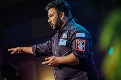 Dwayne Fernandes, wearing a space-themed flight suit, presenting passionately on stage at Accessibility & Inclusion 2025, gesturing with intensity.